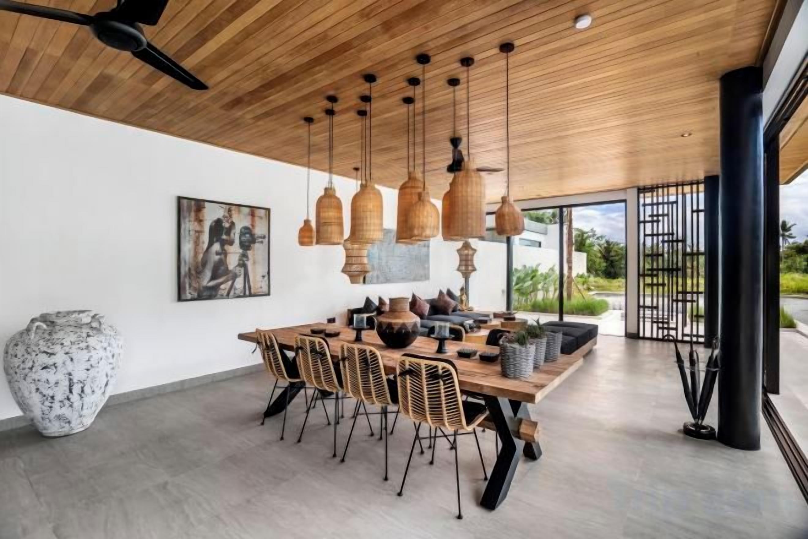 A modern dining area with a wooden ceiling, hanging pendant lights, a large dining table, and chairs.