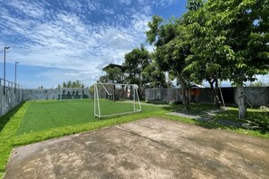 Un espacio al aire libre cercado con suelo de concreto, un arco de fútbol y árboles.