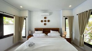 Une chambre d’hôtel avec un grand lit, deux tables de chevet, un appareil de climatisation et des rideaux aux fenêtres.