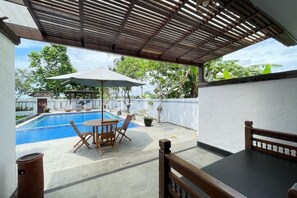 Une terrasse couverte avec une piscine, des sièges d’extérieur et une vue sur la végétation environnante.
