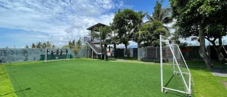 A grassy outdoor area with a goalpost, trees, and a building in the background.