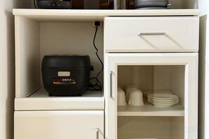 A white cabinet with a rice cooker on the top shelf and a glass-fronted cabinet below containing stacked plates. - TAKAYAMA KAEDENOYADO (Takayama)