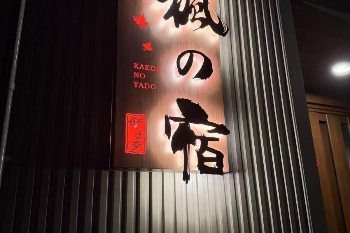 A vertical sign with Japanese characters and English text 'KAEDEN NO YADO' against a backdrop of vertical blinds.