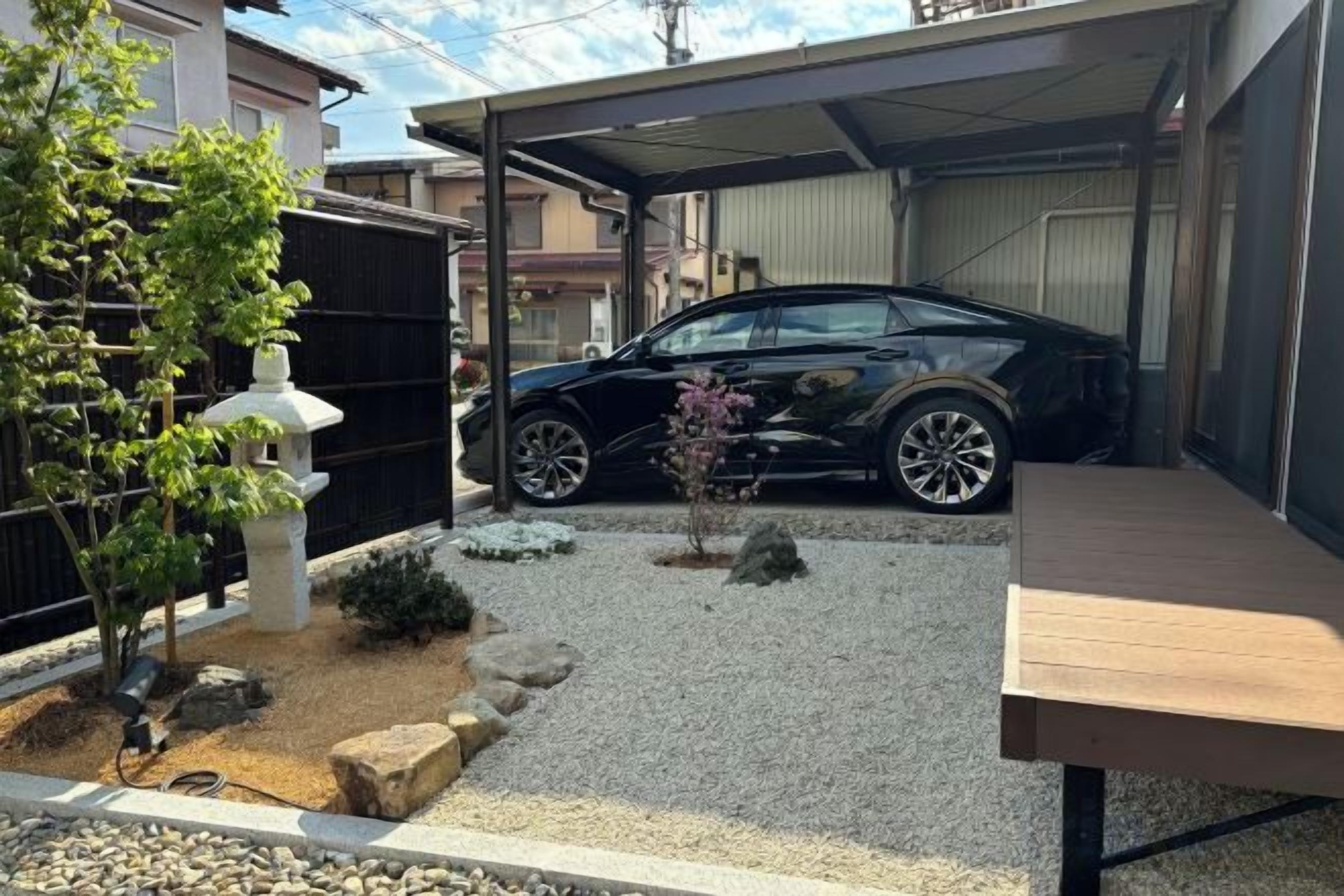 Une voiture noire garée dans un garage fermé, une allée gravillonnée et un banc en bois.
