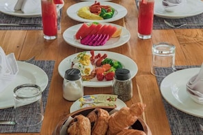 A breakfast setting with plates of food, including eggs, meats, and vegetables, and two glasses of red juice. - 3 Bedroom Villa Ascarya (Bali)
