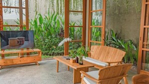 Un espace extérieur aménagé en bois, avec un téléviseur, une table et des chaises, le tout entouré d’une végétation luxuriante.