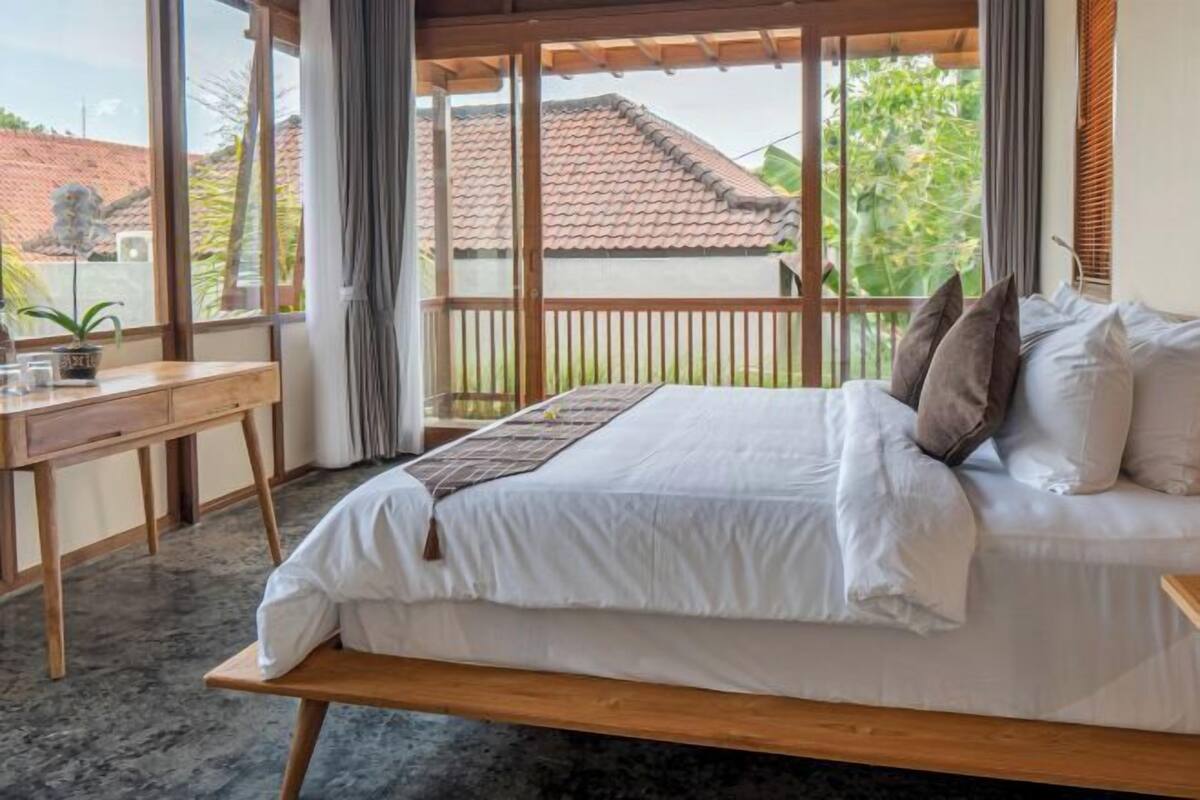 Een slaapkamer met een bed, een houten bureau en uitzicht.