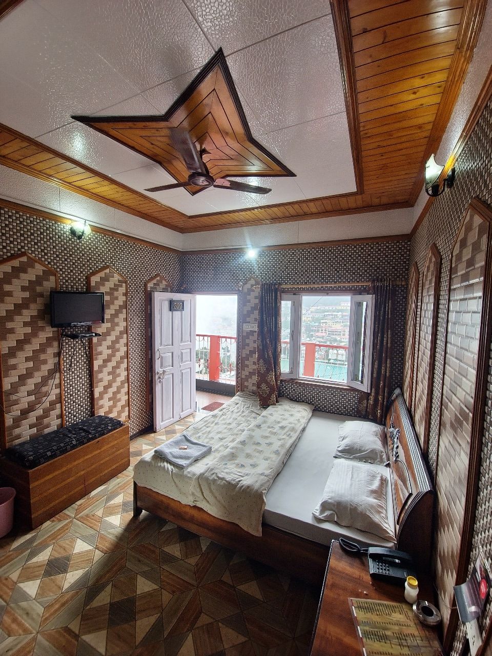 Una habitación pequeña con cama, una mesita, una silla, una ventana y un ventilador de techo.