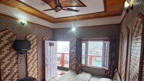 Ein kleines Zimmer mit Bett, einem Tisch, einem Stuhl, einem Fenster und einem Deckenventilator.