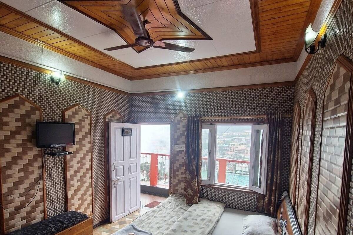 Une petite pièce comprenant un lit, une petite table, une chaise, une fenêtre et un ventilateur de plafond.