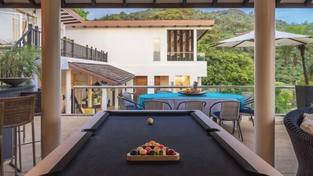 Un área de piscina al aire libre con mesa de billar, sillas y una mesa con fruta.