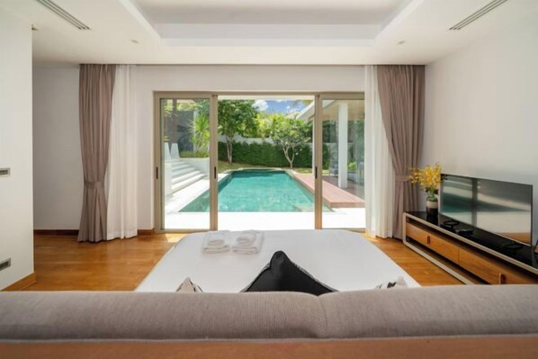 A modern bedroom with a large bed, a TV, and a view of a swimming pool.