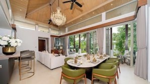 A modern dining area with a round table, green chairs, and a chandelier.
