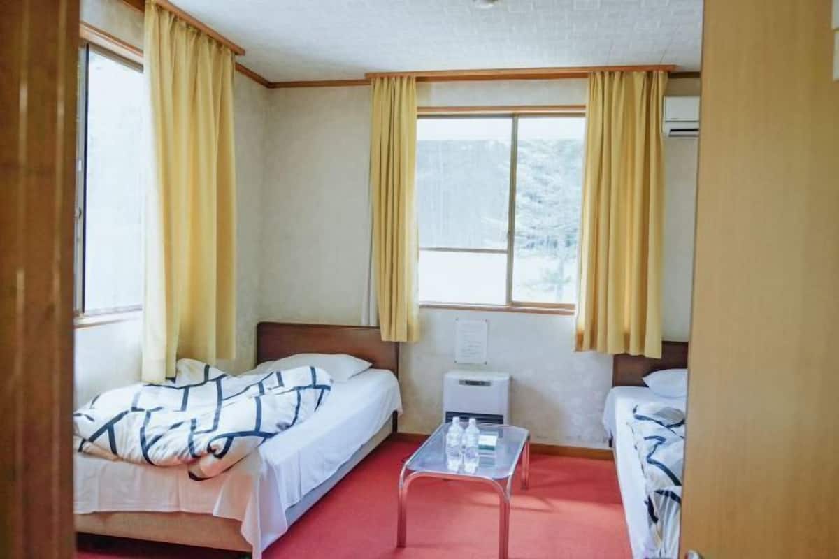 Een hotelkamer met twee bedden, een tafeltje en een raam met gordijnen.