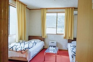 A hotel room with two beds, a small table, and a window with curtains. - FOREST GARDEN HOTEL (Oshino)