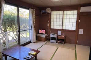 A room with tatami mats, a television, an air conditioner, and a sliding door to a garden. - FOREST GARDEN HOTEL (Oshino)