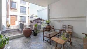 A balcony with a view of neighboring buildings, a wooden table, chairs, and potted plants. - Good Moon at Tha Phae (Chiang Mai)