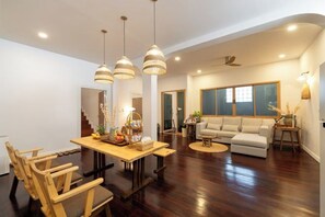 A spacious living area with a wooden dining table, multiple chairs, a sofa, and a coffee table. - Good Moon at Tha Phae (Chiang Mai)