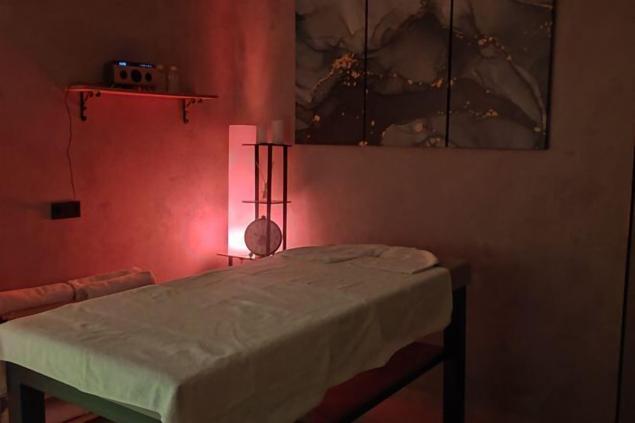 Un cuarto de terapia de masajes con una camilla, un estante con una radio y un cuadro en la pared.