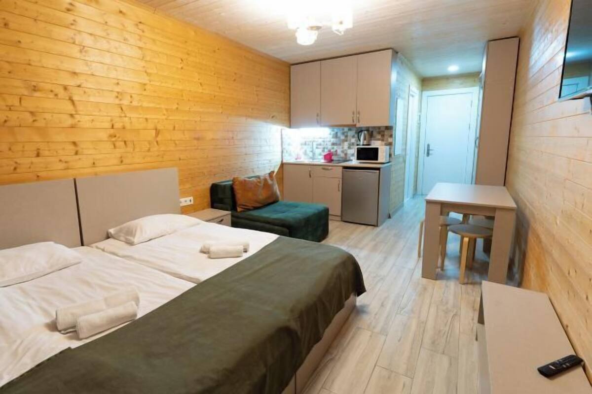 A room with two beds, a small kitchenette, and a desk.