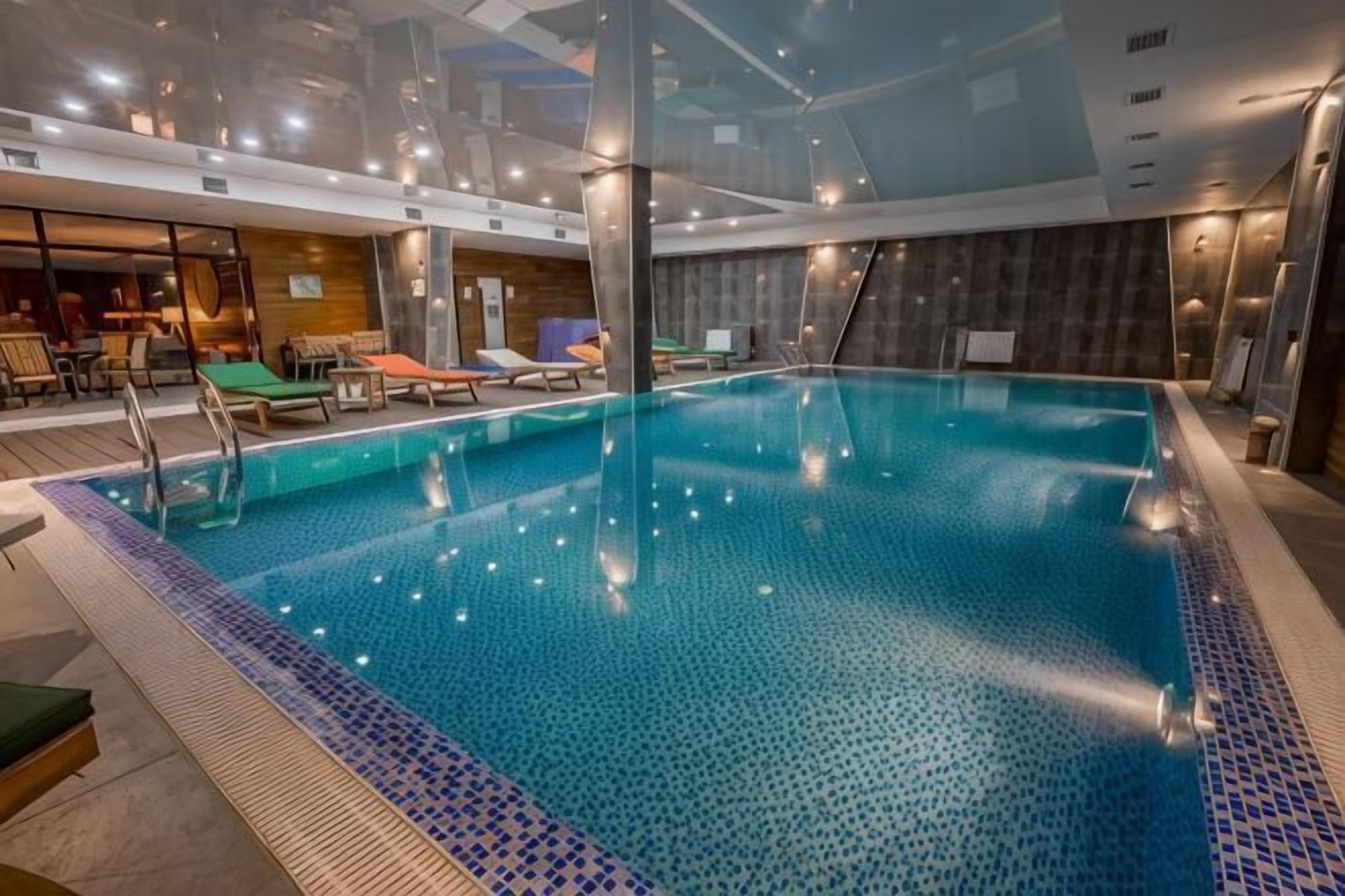 Een binnenzwembad met helder water, ligbedden en een modern interieur.