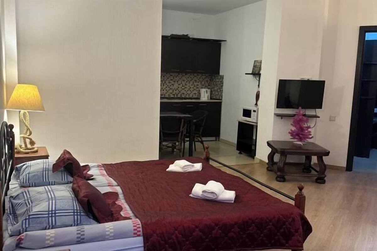 A hotel room with a bed, a desk, a chair, a TV, and a small table with a decorative item.