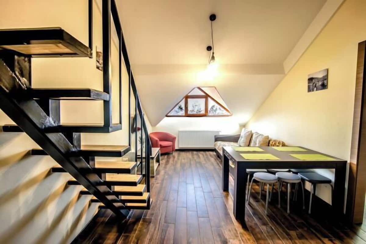 A loft-style room with a wooden staircase, a dining area with a table and chairs, and a red chair.
