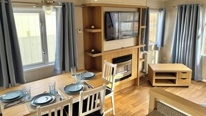 A modern kitchen with a built-in TV, wooden cabinets, and a dining area set for four. - Mobile home Seehund at the Geiseltalsee (Mücheln (Geiseltal))
