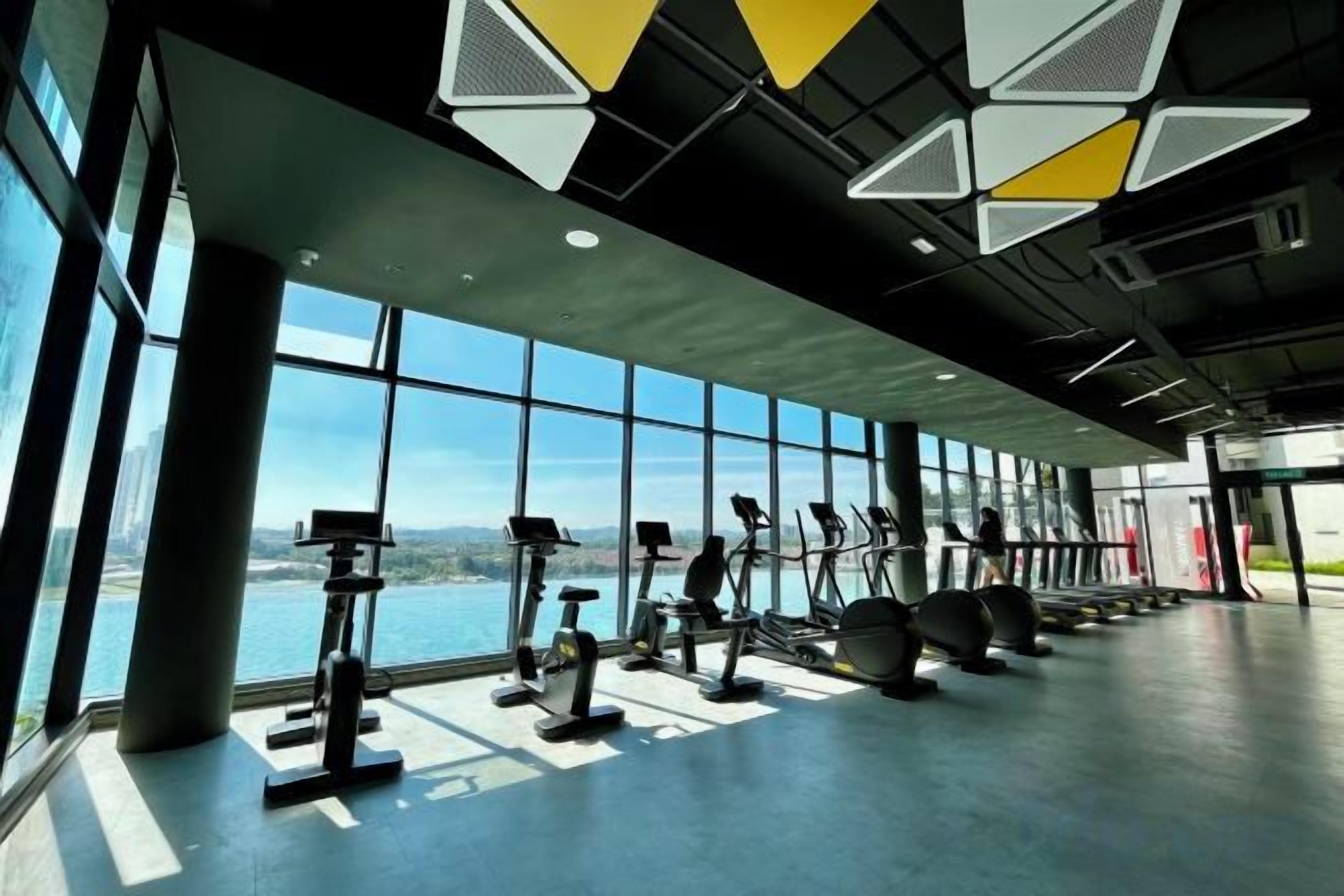 A gym with exercise equipment and large windows overlooking a body of water.
