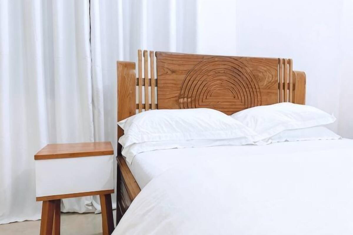 Un lit avec une tête de lit en bois, un oreiller blanc et un couvre-lit blanc.
