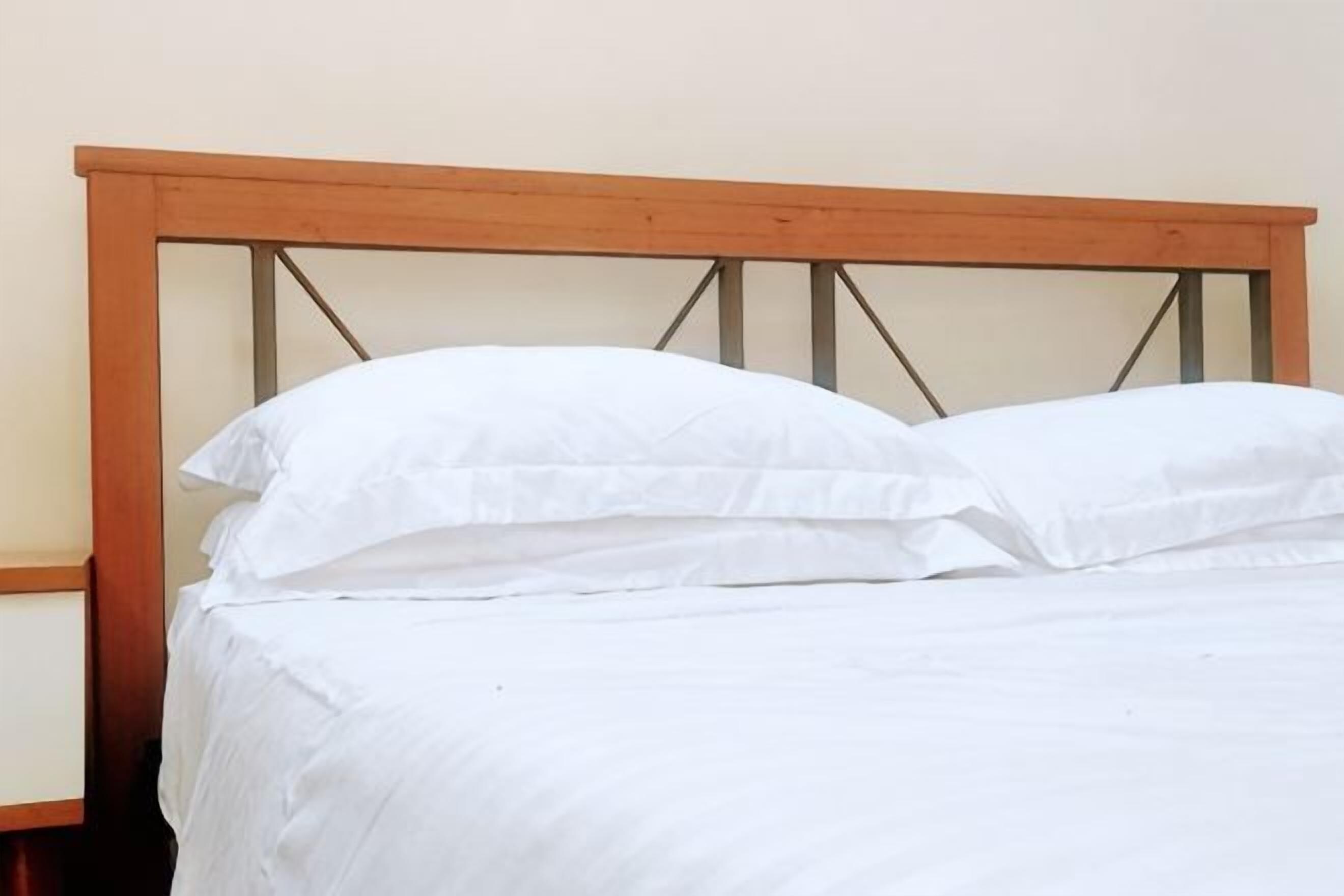 Cama com roupa de cama branca e cabeceira de madeira.