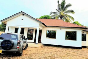 A single-story building with a tiled roof, a covered porch, and a parked car. - Elrad Msamvu Villa with Privacy by Monalisa (Morogoro)