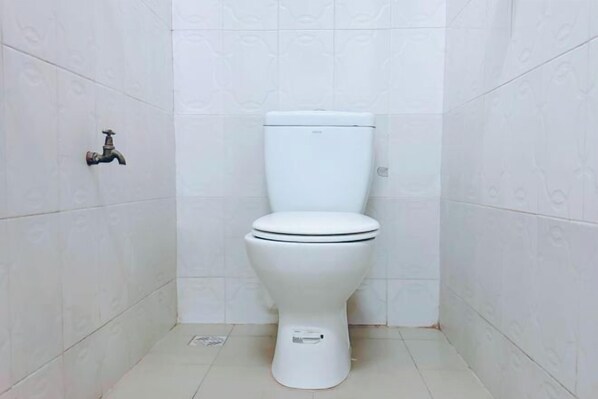 Des toilettes blanches dans une salle de bain dont les murs et le sol sont recouverts de carreaux blancs à motifs.
