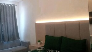 A bedroom with a bed, a nightstand, a lamp, and a window with curtains. - APARTEMEN TRANSPARK JUANDA BEKASI by ilfal (East Bekasi)