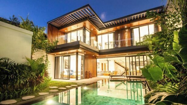 Ein modernes, zweistöckiges Haus mit einem überdachten Pool, umgeben von üppiger Vegetation.