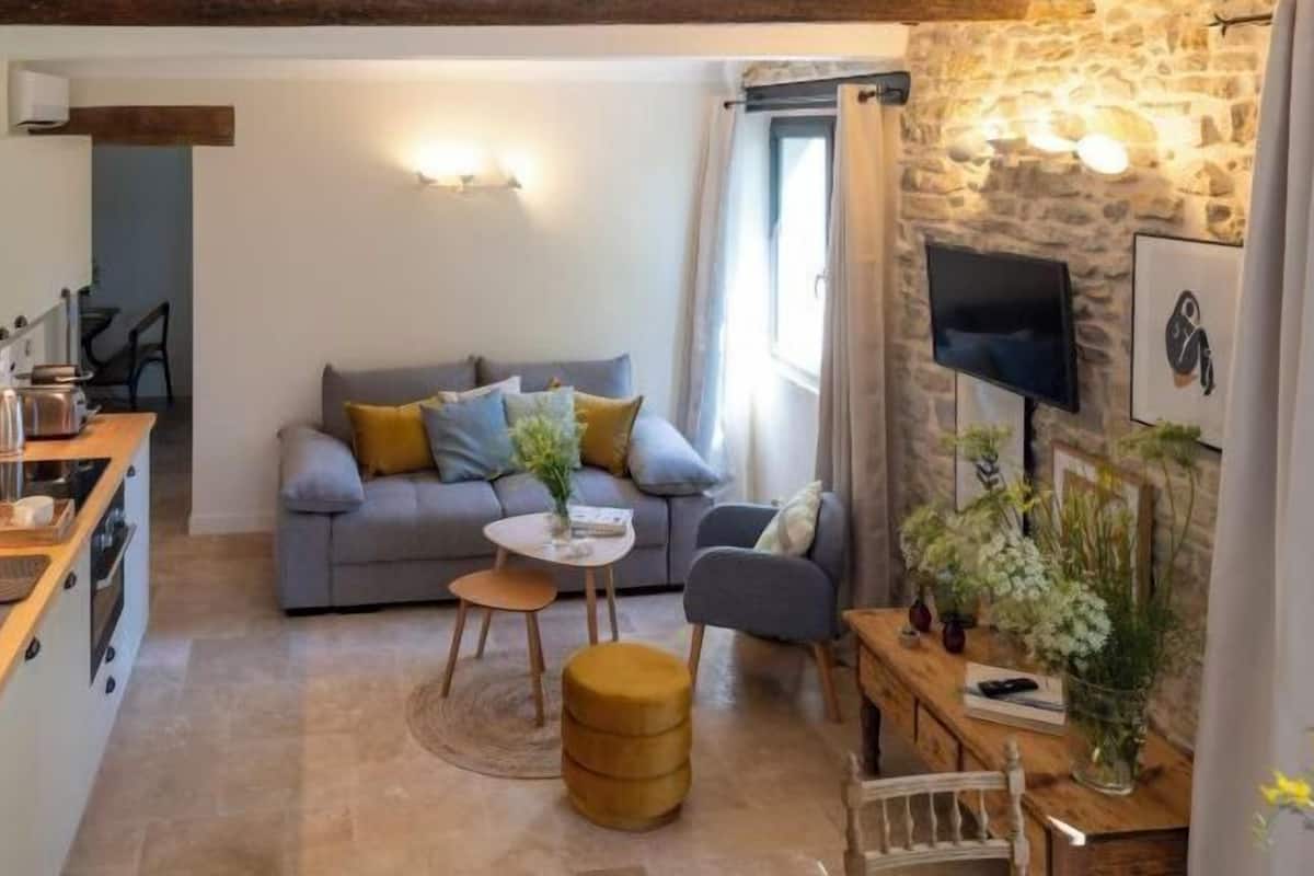 Un salon chaleureux avec un canapé, une table basse et un téléviseur fixé au mur, qui est en pierre.