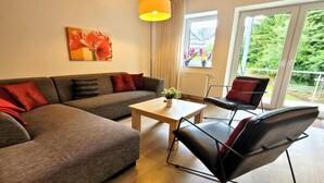 A modern living room with a sofa, a coffee table, and a chair. There is a window with a view of greenery outside. - Bright Stay in Central Winterberg (Winterberg)