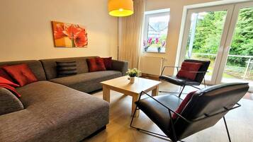 Una sala de estar moderna con un sofá, una mesa de centro y un sillón. Se ve un ventanal con vistas a áreas verdes.