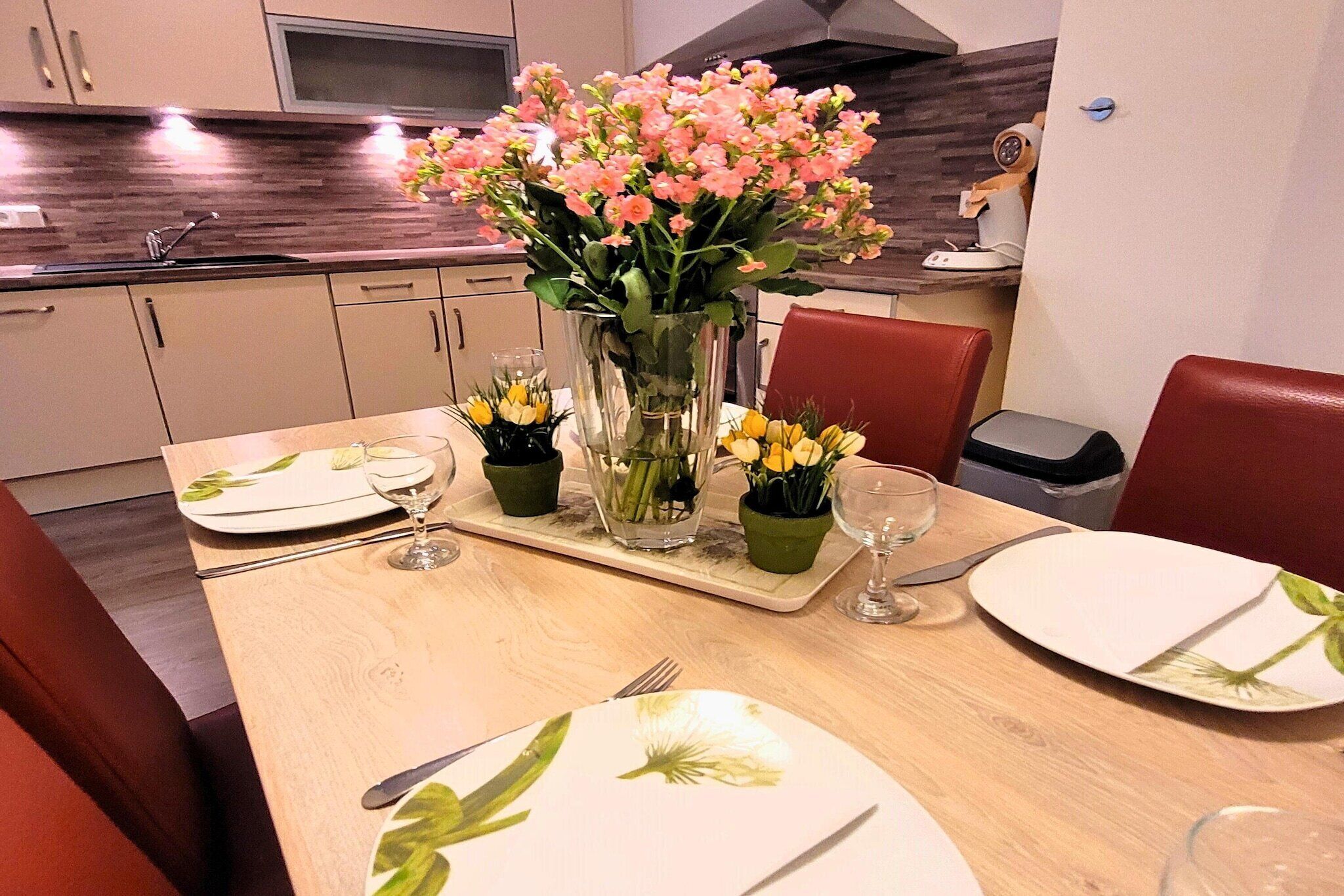 Una mesa de comedor lista con platos, cubiertos y un jarrón de flores.