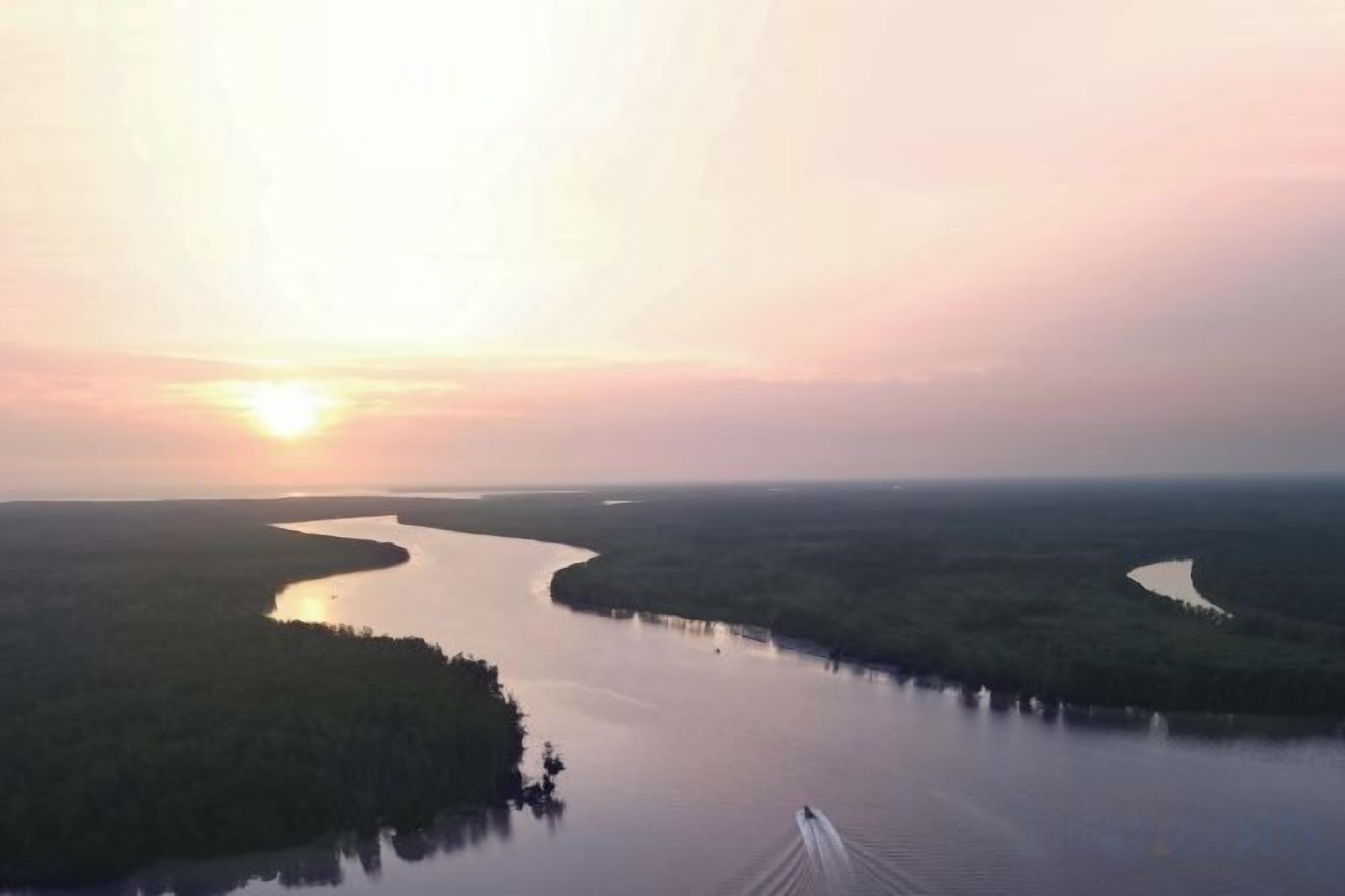 Un río serpentea por un paisaje boscoso, con una embarcación en primer plano.