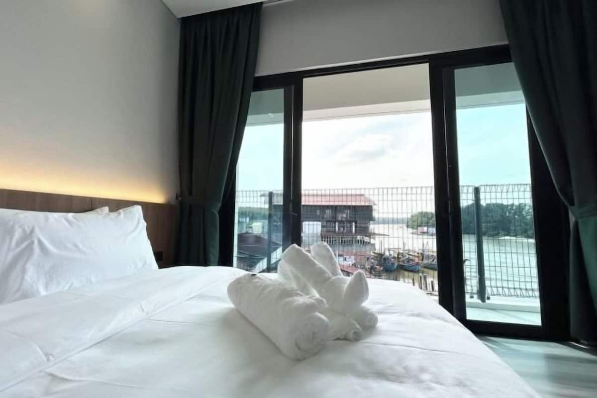 A hotel room with a large bed, a view of a building and a body of water through the window.
