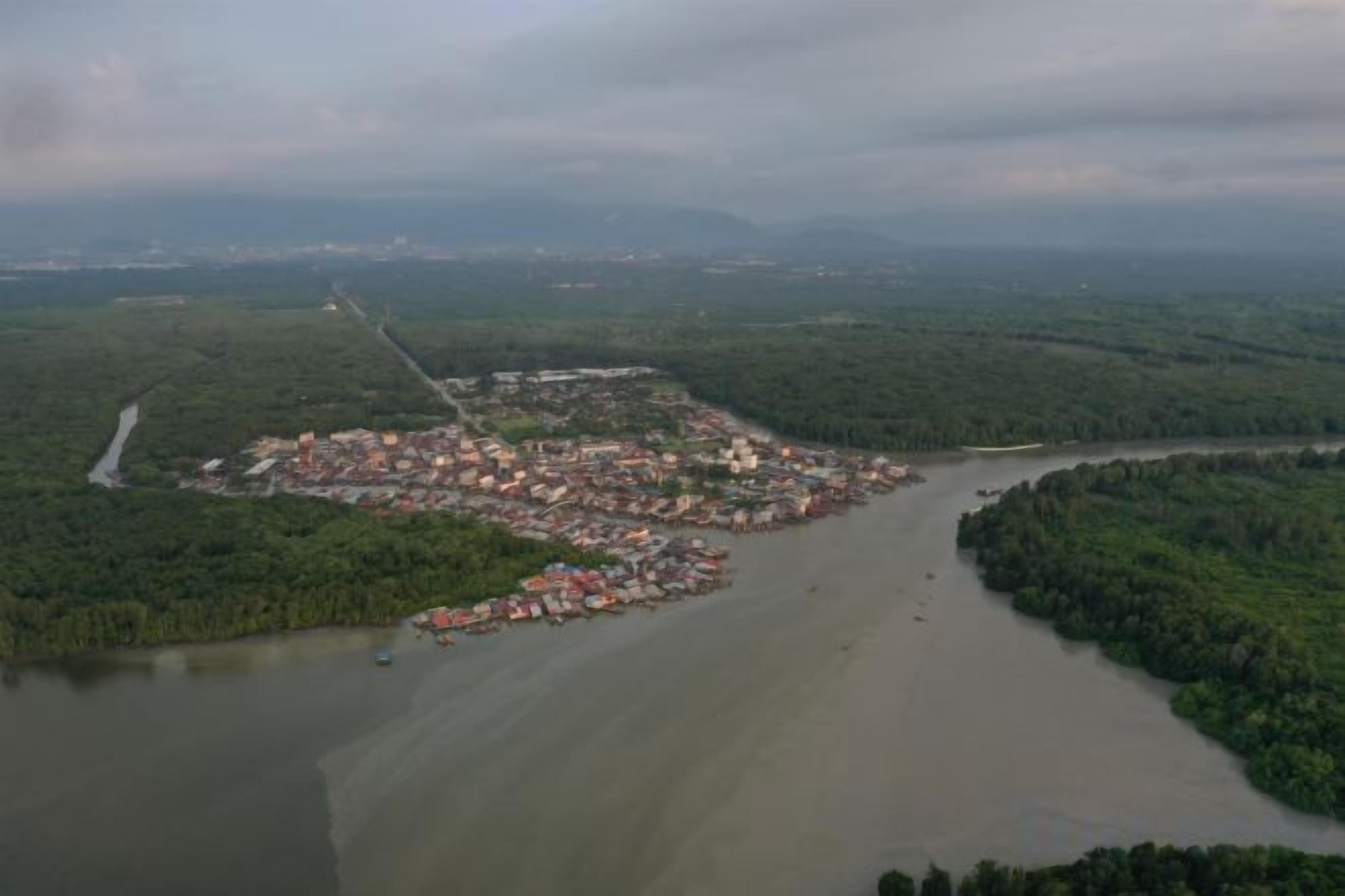 An aerial view of a coastal town with a river, dense greenery, and a mix of residential and commercial buildings.