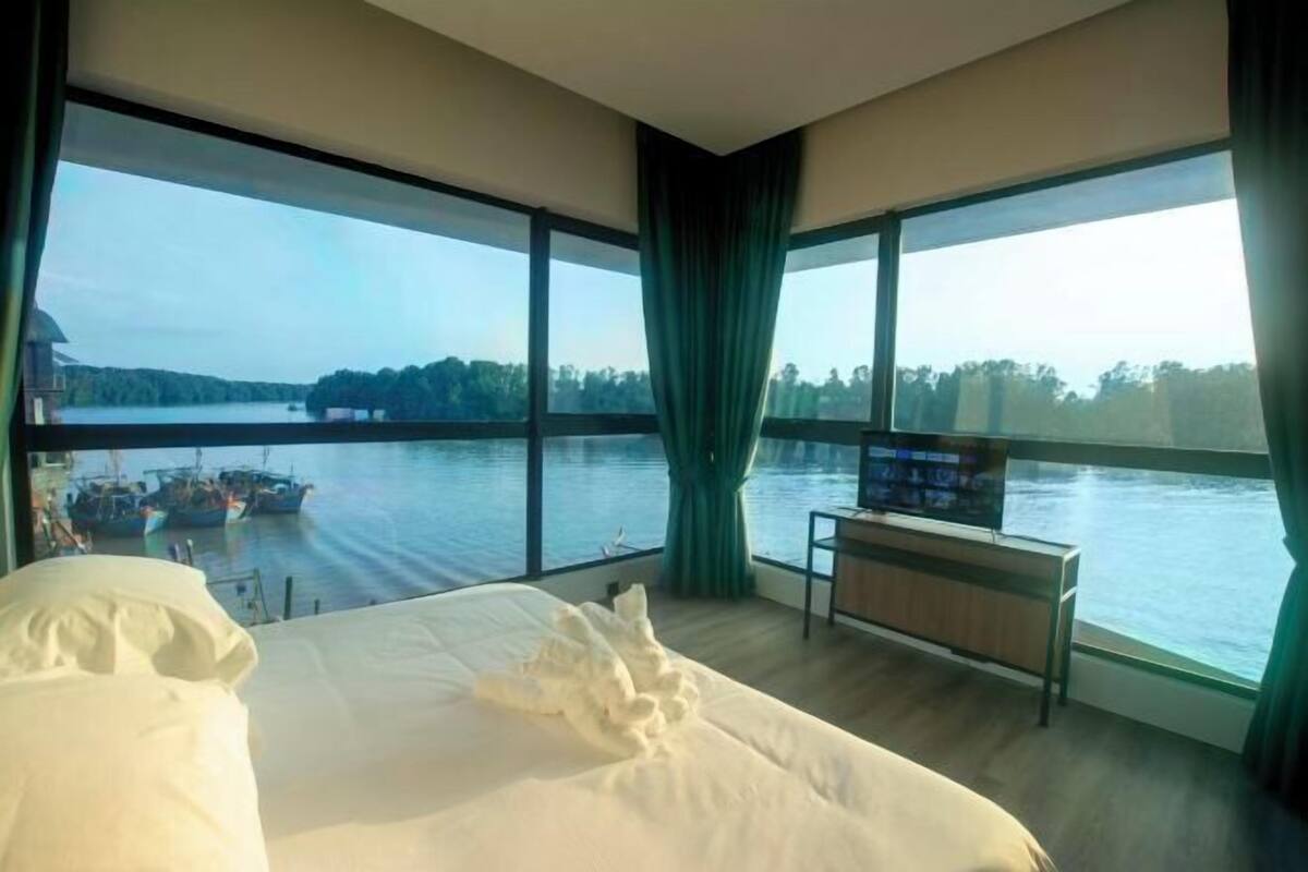 A hotel room with a large bed, a TV, and a view of a body of water with boats.