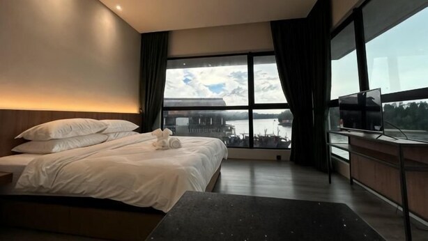 A modern hotel room with a large bed, a desk with a computer, and a large window offering a view of the city. - Crosview (Kuala Sepetang)