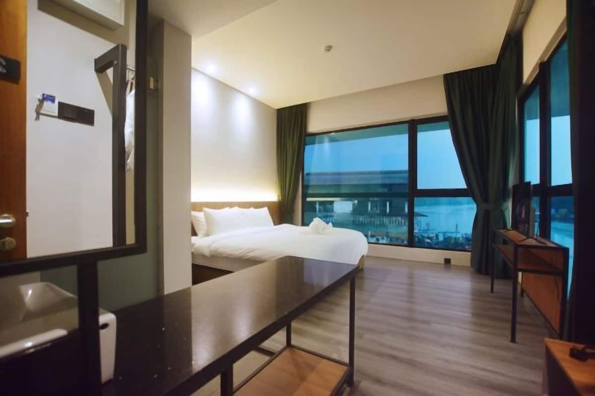 A hotel room with a bed, a desk, a chair, a window with a view, and a door.