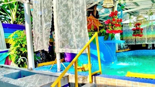 A swimming pool with a blue and yellow color scheme, surrounded by plants and a tiled area. - DMI Hotels and Apartments with Newly opened Lava Stone Pool by Reddoorz (Tabaco)