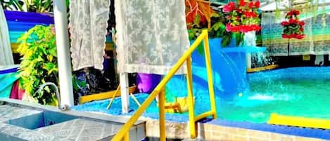 Un área de piscina con una fuente de agua azul, un pasamanos amarillo y flores rojas.
