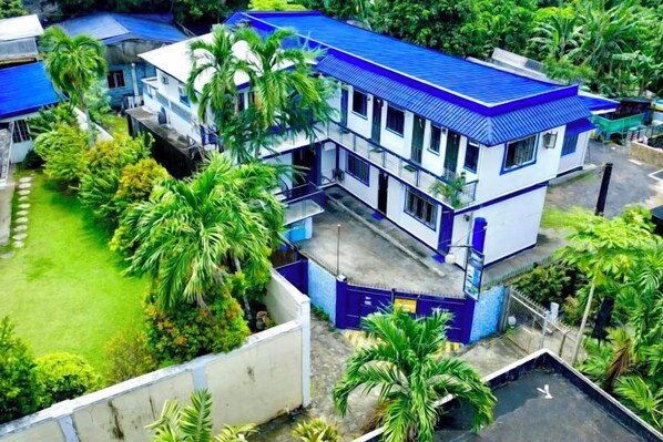 Un edificio de varios pisos con techo azul, rodeado de vegetación y palmeras.