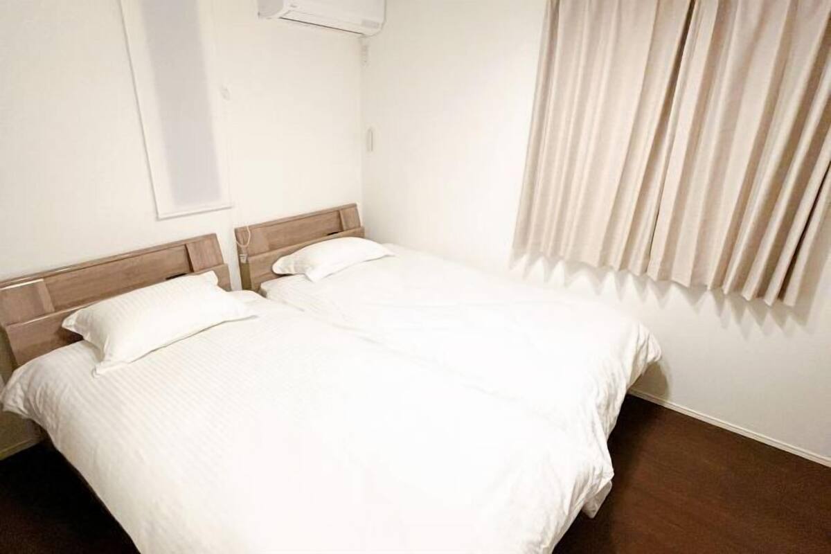 A room with two beds, a wooden headboard, a window with blinds, and a curtain.