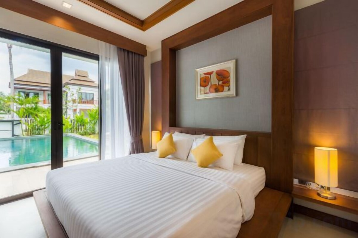 A hotel room with a large bed, a nightstand, a lamp, and a view of a swimming pool.